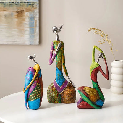 Trio of colorful abstract resin statues with silver-look heads, each in a unique artistic pose and vibrant patchwork design, displayed on a white table with modern decor