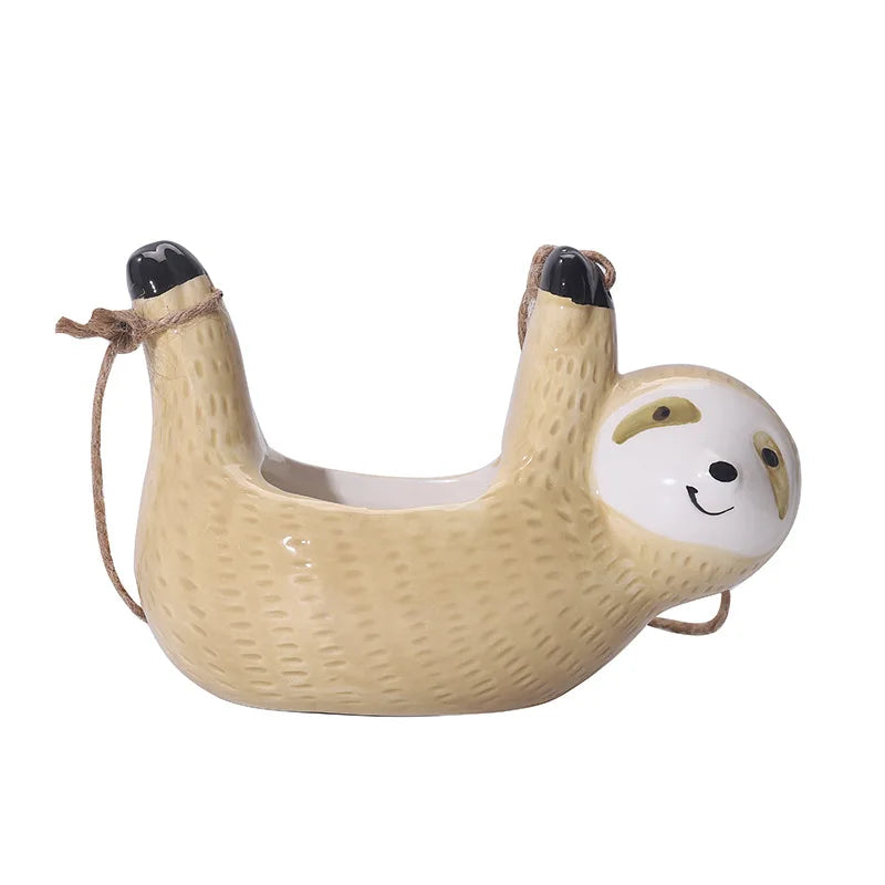 Yellow ceramic sloth hanging planter with a smiling face, black-tipped paws, and attached rope for hanging; designed for small indoor plants or succulents.

