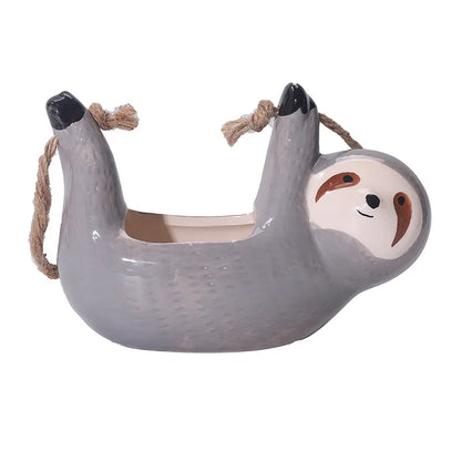 Gray ceramic sloth hanging planter featuring a smiling face, black-tipped paws, and natural rope handles; designed for succulents or small indoor plants.
